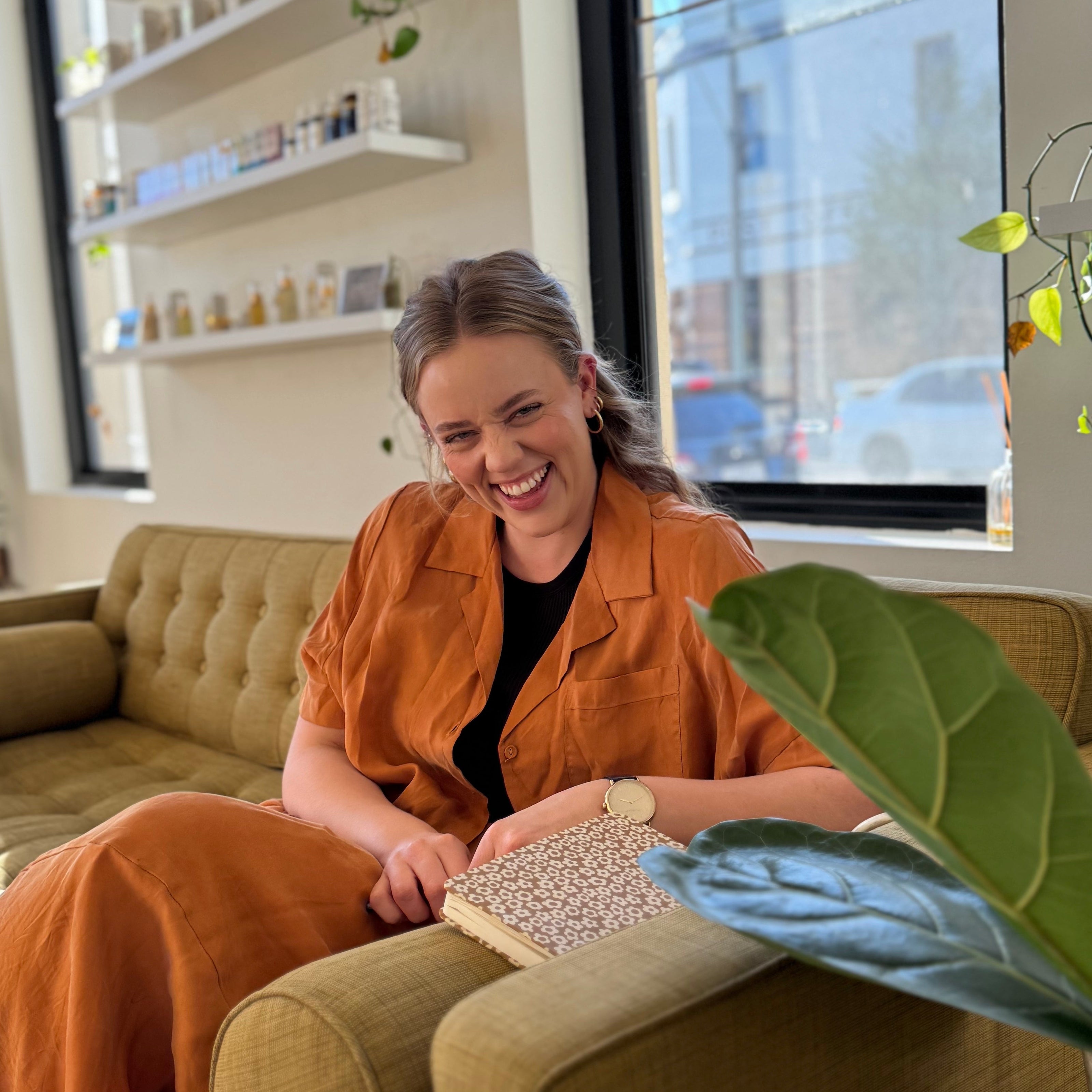 Dr Tahya (TCM) Woman sitting on a couch in a modern living room with large windows.