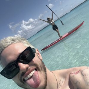 Pete Davidson poking out tongue with sunnies on his face in a blue ocean enjoying himself